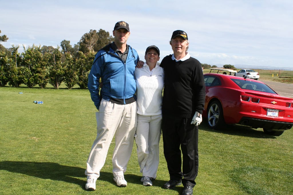 Three People Standing on Golf Course with A Couple of Cars in the Back